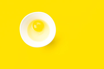 Raw egg in bowl on yellow background. Healthy food and cooking at home concept.