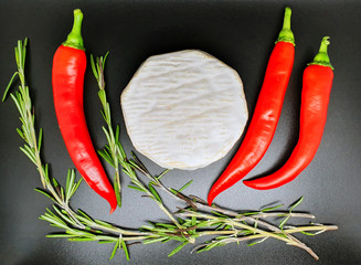 composition of white-mold camembert cheese, red hot chili peppers and thyme twigs, on a black background