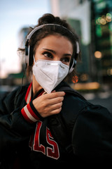 Fototapeta na wymiar young girl dressed in sport wears medical mask on city street