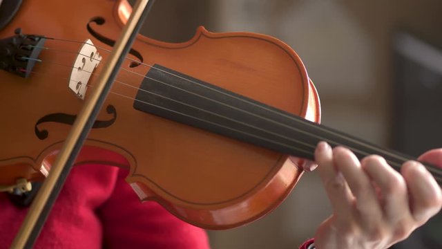 Young woman playing the violin. Bow movement along the strings, close up view.