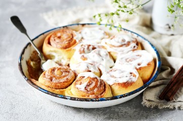 Cinnamon buns in a baking dish with cream cheese curd on a gray background