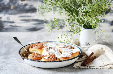 Cinnamon buns in a baking dish with cream cheese curd on a gray background