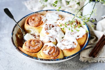 Cinnamon buns in a baking dish with cream cheese curd on a gray background
