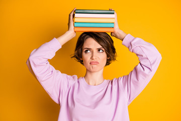 Portrait of frustrated upset girl hold pile stack textbooks on her head she need read for lesson...
