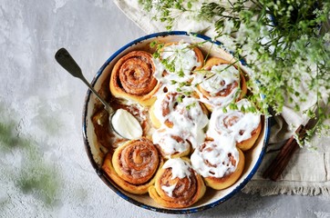 Cinnamon buns in a baking dish with cream cheese curd on a gray background