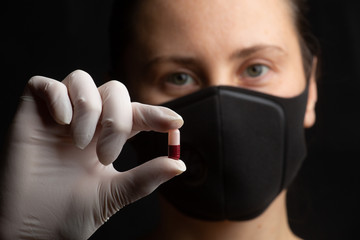 Close-up, selective focus, a girl in a protective face mask holds a pill in her hand. Medication concept. Coronavirus, Covid-19.