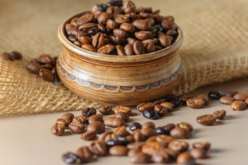 A pot of coffee beans on a sacking. Roasted coffee beans are scattered on the table. A mix of different types of coffee roasting.
