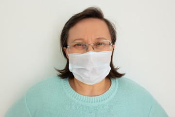 Mature woman wearing casual, glasses and medical face mask, posing isolated against white background. Closeup, front view. Epidemic or virus concept