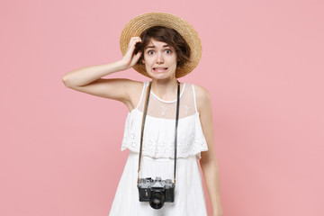 Puzzled concerned young tourist girl in summer white dress hat with photo camera isolated on pink...