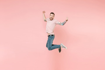 Fototapeta na wymiar Side view of excited young tattooed man guy in pastel casual t-shirt posing isolated on pink background. People lifestyle concept. Mock up copy space. Jumping, doing winner gesture, looking camera.