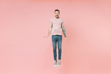 Surprised young tattooed man guy in pastel casual t-shirt posing isolated on pink wall background studio portrait. People sincere emotions lifestyle concept. Mock up copy space. Jumping having fun.