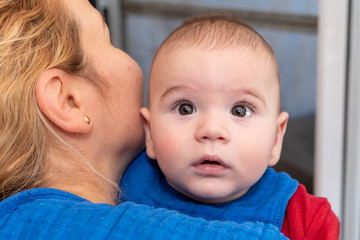 Cute 6 months little baby boy with curiosity expression on his face in his mothers arms