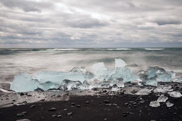 Melting Ice chunks getting washed on shore on black lava icy beach in diamond beach in iceland. Global warming and climate change concept.