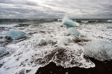 Melting Ice chunks getting washed on shore on black lava icy beach in diamond beach in iceland. Global warming and climate change concept.