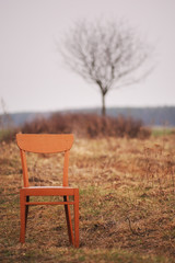 Red vintage, rustic, wooden chair in a field in early spring.