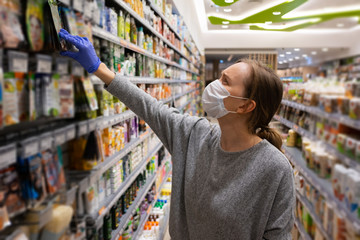 Female customer wearing mask and gloves, choosing food in supermarket. Woman in grocery store. Medium shot. Shopping during epidemic concept