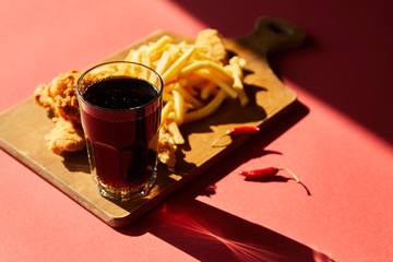 selective focus of spicy deep fried chicken and french fries served on wooden cutting board with soda in sunlight