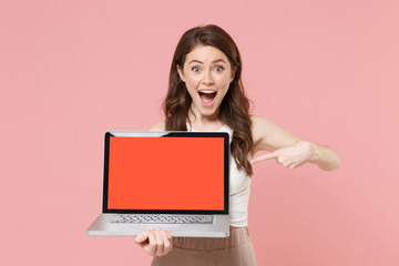 Naklejka premium Excited young woman girl in light casual clothes isolated on pastel pink background. People lifestyle concept. Mock up copy space. Pointing index finger on laptop pc computer with blank empty screen.
