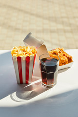selective focus of tasty deep fried chicken, french fries and soda in glass on white table in sunlight near window