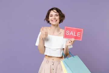 Smiling young woman girl in summer clothes isolated on violet background. Shopping discount sale concept. Mock up copy space. Hold package bag with purchases sign with SALE title showing thumb up.