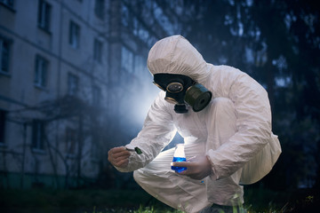 Crouching scientist working in uniform and a gas mask, found a sample for his laboratory study in zone of high danger, concept of polluted environment