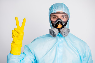 Portrait of medical worker man in white hazmat uniform breathing mask make v-sign isolated over gray color background