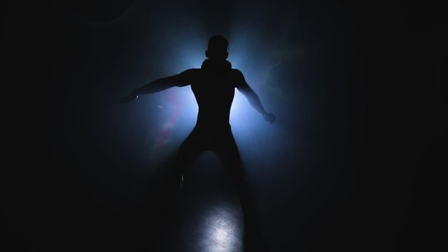 Young muscular and sexy man dancing in the shadow on the background of a spotlight