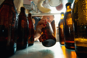 Caucasian woman takes cold refreshing beer from out the fridge, inside view from fridge of hand...