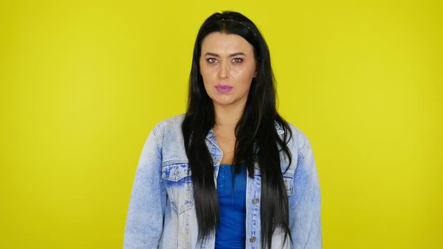 Angry woman with black hair in a denim jacket shows a fist at the camera on yellow background with copy space. Place for text or product. 4K footage