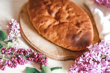 Homemade Apple pie on a wooden table next to a bowl of lilacs. Gentle toning.
