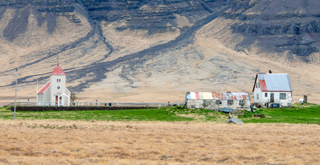 Old and abandoned village in Iceland under the big volcanic snow covered mountains. Church and weathered shack stands next to each other.