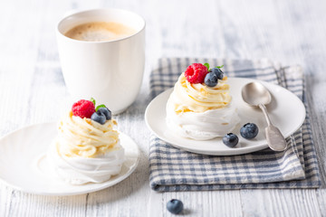 Romantic spring romantic breakfast. Delicious Pavlova cake with cream and fresh berries and mug with coffee. Soft focus