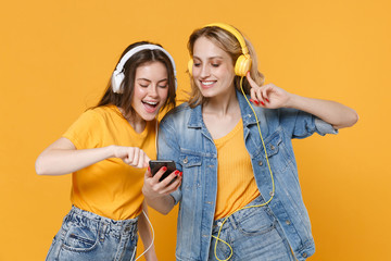 Two cheerful young women girls friends in casual t-shirts denim clothes isolated on yellow...