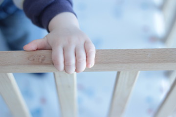 Palm hand of a small baby in a baby cot. Holding to it. Reaching something.