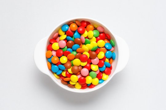 Colorful chocolate candy pills in bowl isolated on white background. Top view