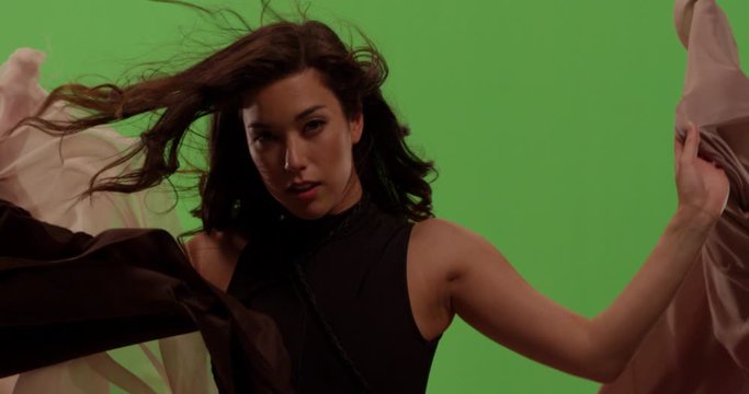 Close up of woman against green screen surrounded by flowing fabric with hair blowing in the wind