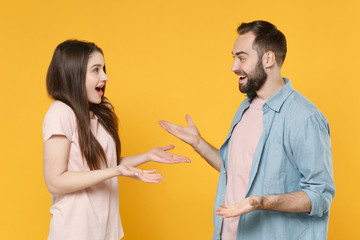Side view of shocked young couple two friends guy girl in casual clothes posing isolated on yellow background. People lifestyle concept. Mock up copy space. Looking at each other, speaking talking.