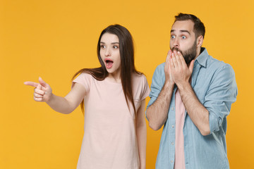 Shocked young couple two friends guy girl in casual clothes posing isolated on yellow background. People lifestyle concept. Mock up copy space. Pointing index finger aside, covering mouth with hands.