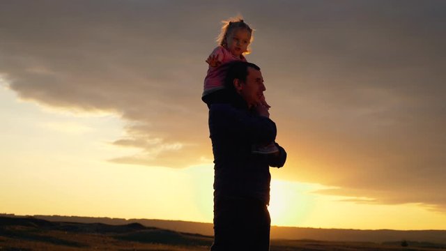 Silhouette of a happy family at sunset. The daughter sits on the shoulder of her father and depicts the flight of an airplane. The family is relaxing in the fresh air, dreaming of traveling.