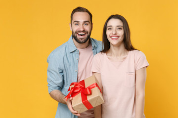 Excited young couple two friends guy girl in casual clothes isolated on yellow background. Valentine's Day, International Women's Day, birthday, holiday concept. Hold present box with gift ribbon bow.