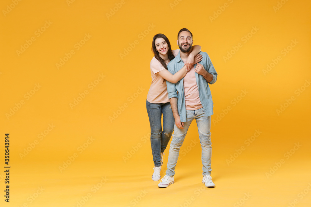 Wall mural Funny young couple two friends guy girl in pastel blue casual clothes posing isolated on yellow wall background studio portrait. People lifestyle concept. Mock up copy space. Hugging, looking camera.