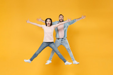 Fototapeta na wymiar Excited young couple two friends guy girl in pastel blue casual clothes posing isolated on yellow background in studio. People lifestyle concept. Mock up copy space. Jumping, spreading hands and legs.