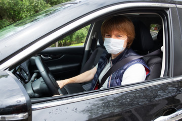 Male car driver wearing face mask, sitting at car wheel, looking at camera. Vehicle side window. Car driver and virus pandemic concept