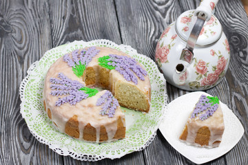 Lavender Cupcake. Sugar coated. Decorated with lavender glaze flowers. A small piece is cut off. Nearby is a kettle.