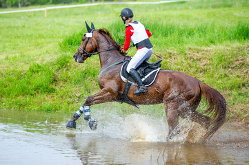 Fototapeta na wymiar Eventing: equestrian rider jumping over an a log fence obstacle in splash