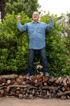 Anziano con camicia in jeans scherza allegramente nel suo giardino urlando sopra una catasta di legna