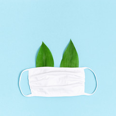 Medical fabric mask with green leaves as ears. Blue background with copy space. Flat lay. Minimal style.