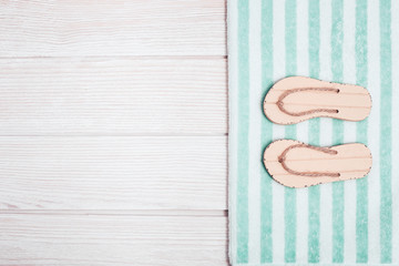 Concept of beach holiday. Beach flip-flops, striped cotton towel. Summer flat lay with copy space. Summer wooden background. Minimal style.