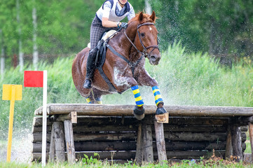 Eventing: equestrian rider jumping over an a log fence water obstacle in splash
