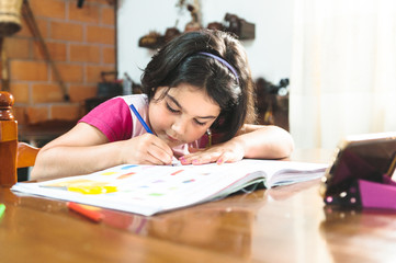 Bambina coni capelli castani fa i compiti a casa sua concentrata su un tavolo di legno